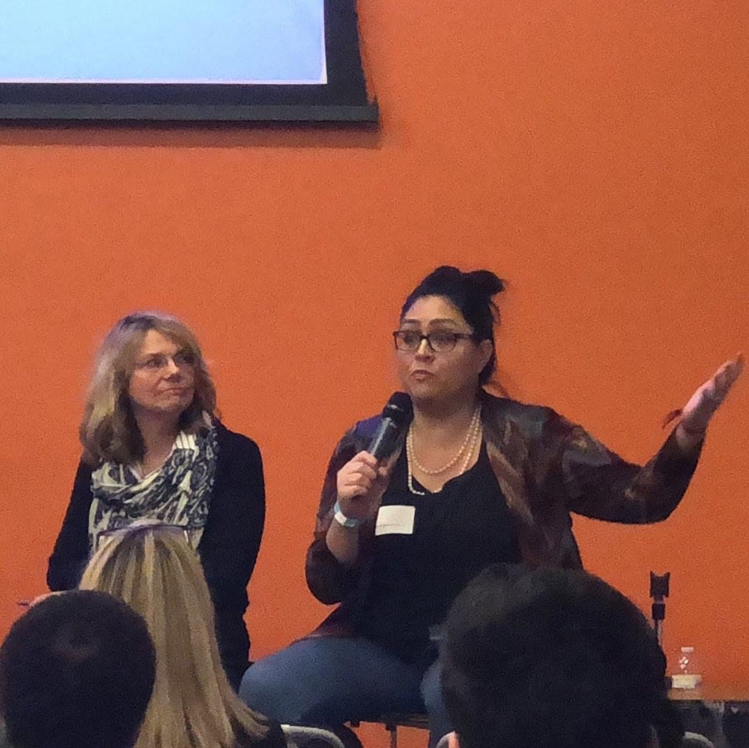 Yamile "Yaya" McBride speaking on a panel, microphone in hand, mid-answer.