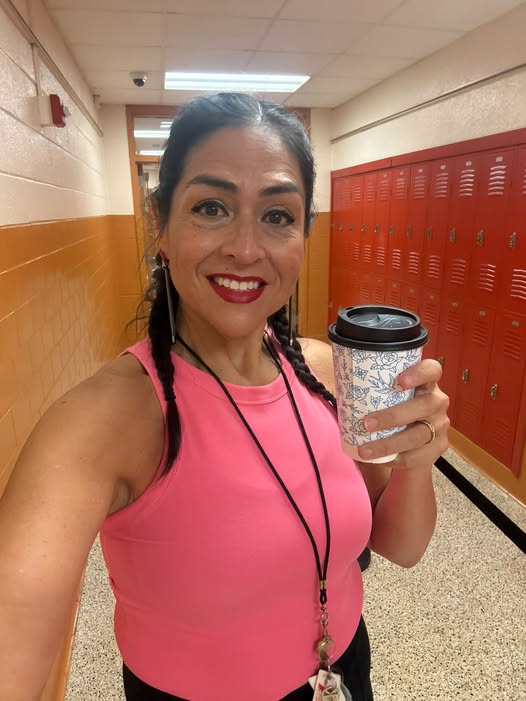 Yamile "Yaya" McBride in a school hallway, holding a coffee, lockers behind her.