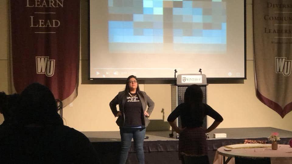Yamile "Yaya" McBride on stage at Winthrop University, addressing an audience beside the podium.